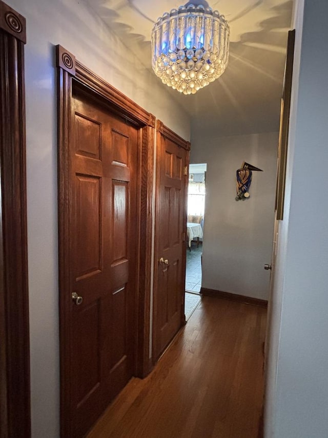 hallway with dark wood-type flooring and a chandelier