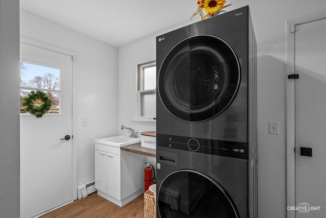 washroom with stacked washer / dryer, sink, cabinets, light hardwood / wood-style floors, and baseboard heating