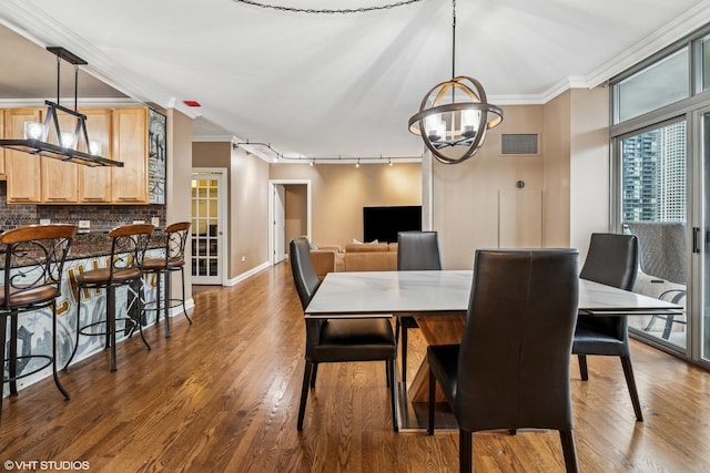 dining area featuring an inviting chandelier, dark wood-type flooring, ornamental molding, and rail lighting