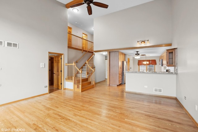 unfurnished living room with a towering ceiling, ceiling fan, and light wood-type flooring