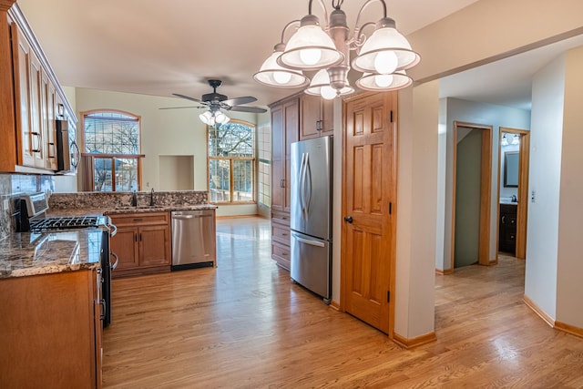 kitchen with sink, light hardwood / wood-style flooring, dark stone countertops, pendant lighting, and stainless steel appliances