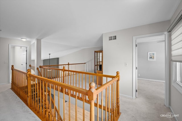 hallway with baseboards, visible vents, light carpet, and an upstairs landing