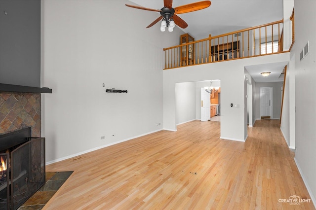 living area featuring visible vents, baseboards, a fireplace with flush hearth, wood finished floors, and ceiling fan with notable chandelier