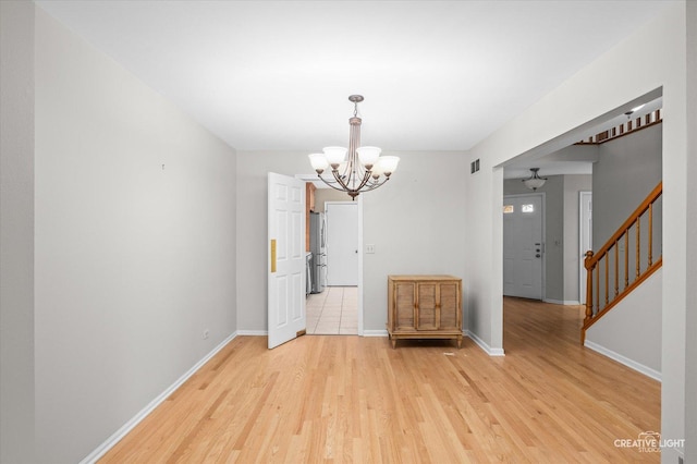 unfurnished dining area with stairs, light wood-type flooring, an inviting chandelier, and baseboards