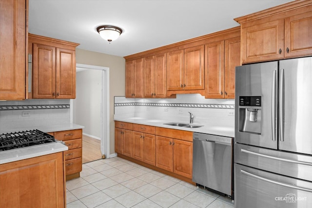 kitchen with stainless steel appliances, a sink, light countertops, decorative backsplash, and brown cabinetry