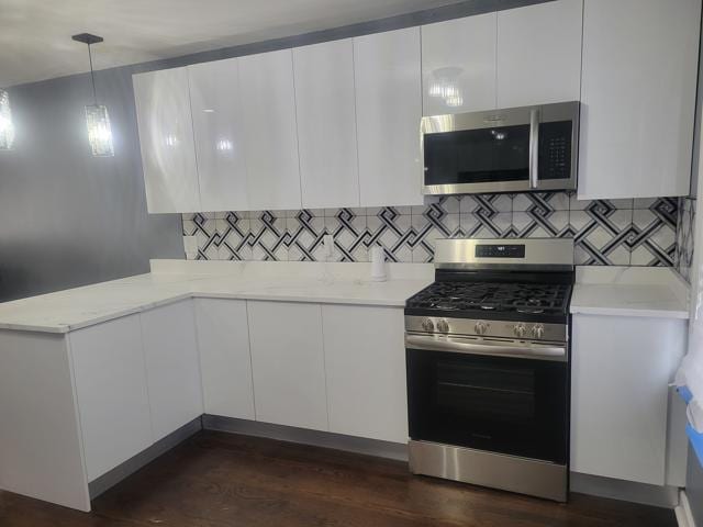 kitchen with white cabinetry, hanging light fixtures, appliances with stainless steel finishes, dark hardwood / wood-style flooring, and backsplash