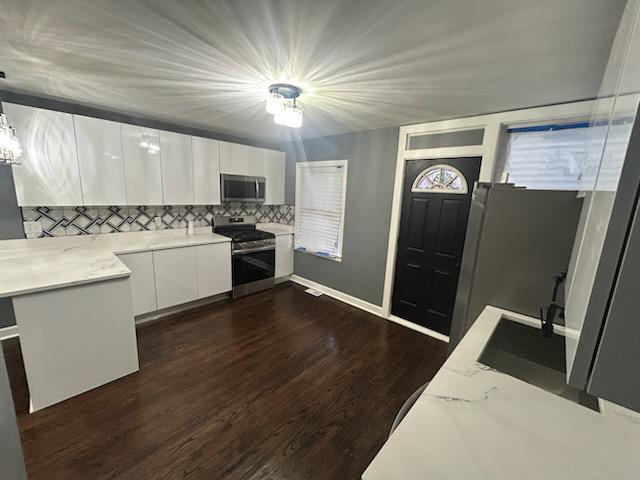 kitchen featuring backsplash, stainless steel appliances, dark hardwood / wood-style floors, white cabinets, and decorative light fixtures