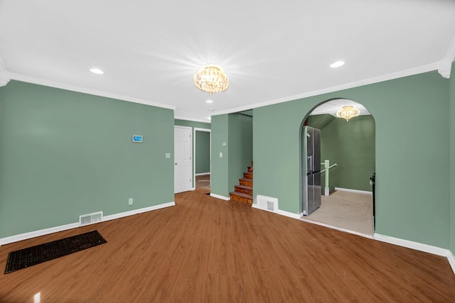 empty room with visible vents, arched walkways, baseboards, and wood finished floors