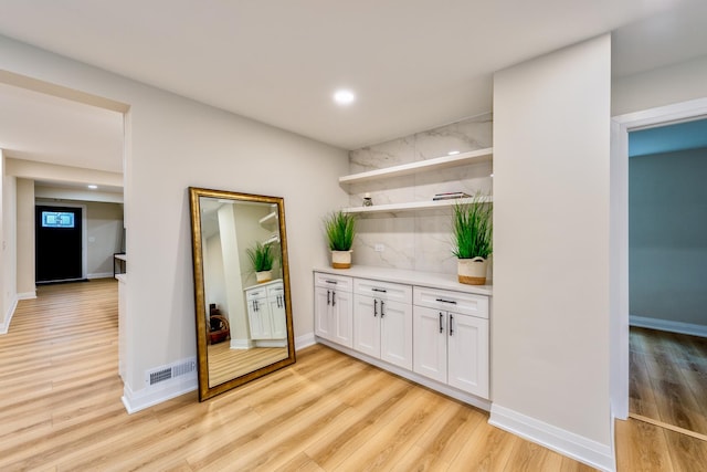 bar with light hardwood / wood-style floors and white cabinets