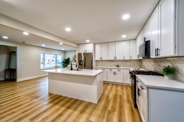 kitchen with sink, stainless steel fridge, white cabinets, a kitchen island with sink, and gas stove