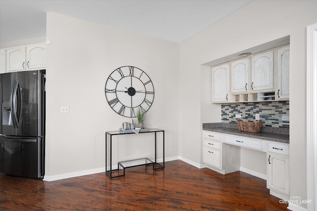 kitchen with black fridge with ice dispenser, backsplash, built in desk, dark countertops, and dark wood finished floors