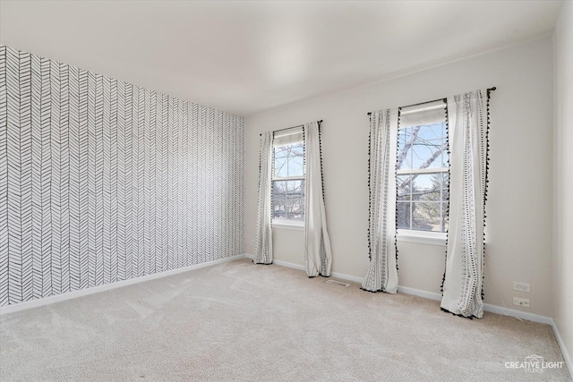 carpeted spare room featuring an accent wall, visible vents, and baseboards