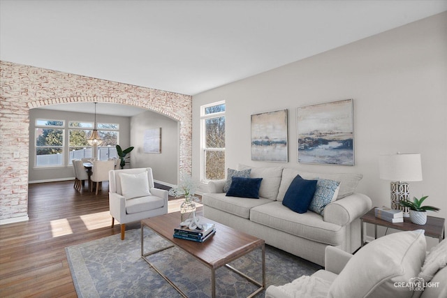 living area with arched walkways, baseboards, wood finished floors, and a chandelier