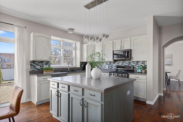 kitchen with arched walkways, dark wood finished floors, decorative backsplash, appliances with stainless steel finishes, and a sink