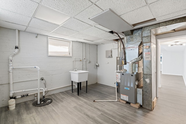 basement with heating unit, hardwood / wood-style floors, and a drop ceiling