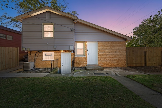 back house at dusk with central AC unit and a yard