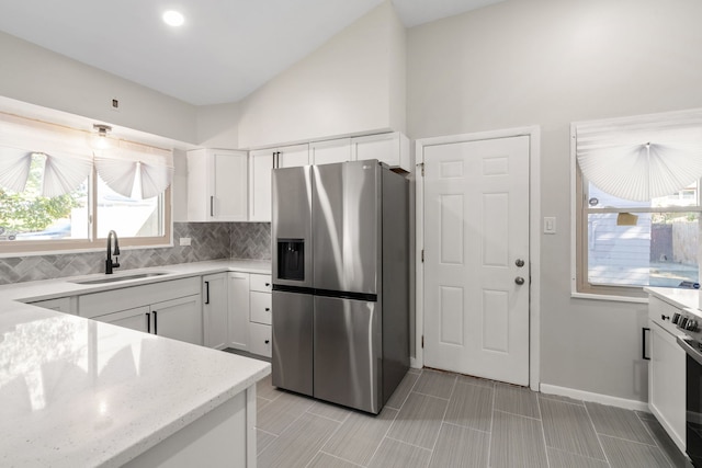 kitchen with stainless steel refrigerator with ice dispenser, sink, white cabinets, and light stone counters