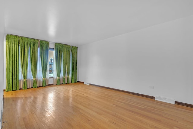 spare room featuring light wood-type flooring, visible vents, and baseboards