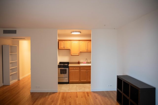 kitchen with stainless steel range with gas cooktop, sink, light brown cabinets, and light wood-type flooring