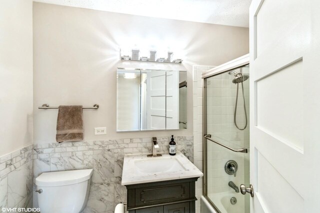 full bathroom with vanity, toilet, combined bath / shower with glass door, and tile walls