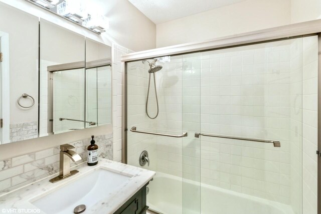 bathroom featuring bath / shower combo with glass door, vanity, and backsplash