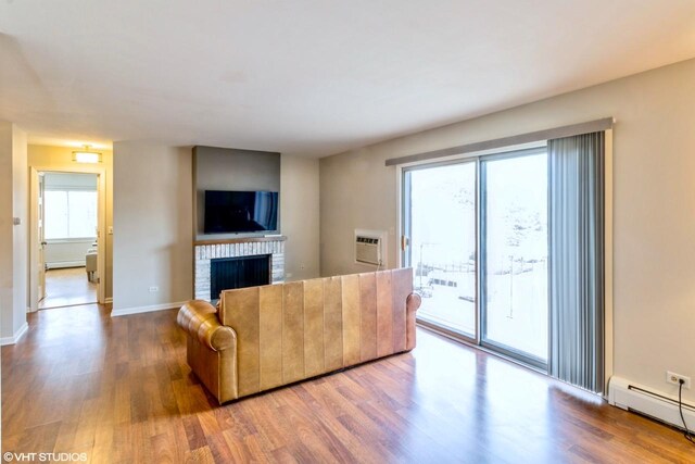 living room with a fireplace, a wall mounted AC, wood-type flooring, and baseboard heating