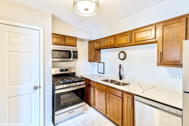 kitchen with appliances with stainless steel finishes, sink, backsplash, and light stone counters