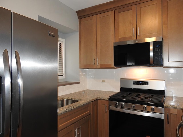 kitchen with tasteful backsplash, light stone countertops, appliances with stainless steel finishes, and sink