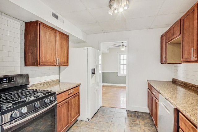 kitchen with a paneled ceiling, dishwasher, light stone counters, tasteful backsplash, and gas range oven