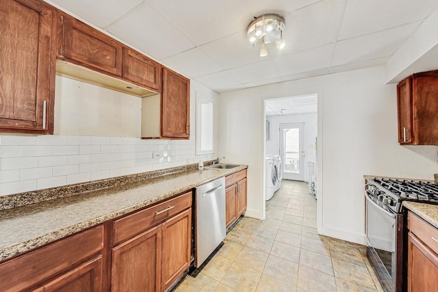 kitchen featuring sink, washer and clothes dryer, range with gas stovetop, decorative backsplash, and stainless steel dishwasher