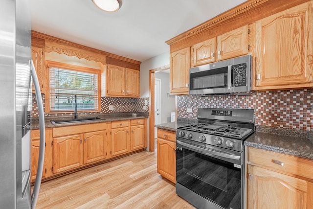 kitchen with sink, dark stone countertops, appliances with stainless steel finishes, light hardwood / wood-style floors, and backsplash