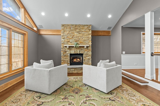 living room with lofted ceiling, hardwood / wood-style flooring, a stone fireplace, and a wealth of natural light