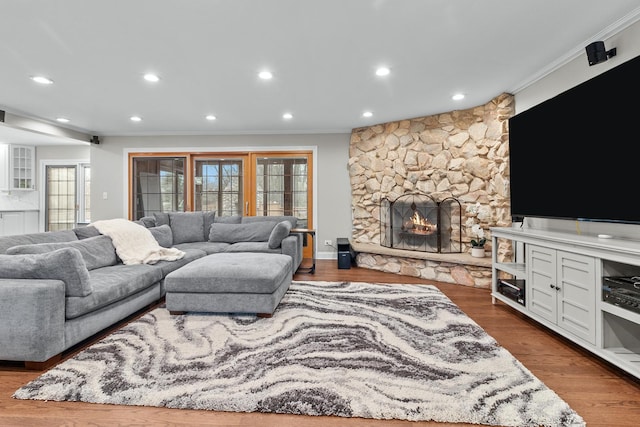 living room with ornamental molding, a stone fireplace, and hardwood / wood-style floors