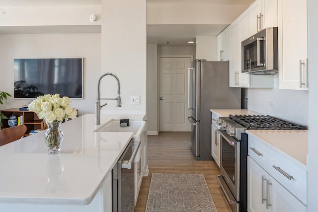 kitchen with stainless steel appliances, backsplash, beverage cooler, light wood-type flooring, and white cabinetry