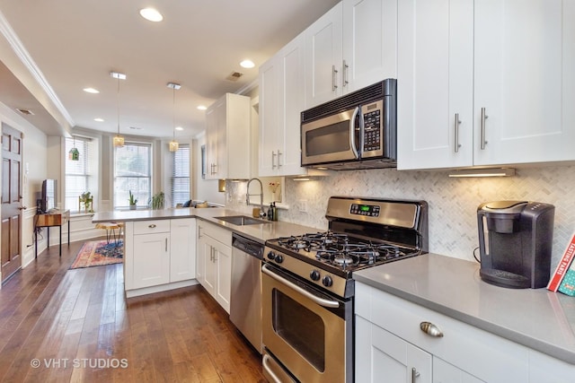 kitchen featuring kitchen peninsula, hanging light fixtures, sink, appliances with stainless steel finishes, and white cabinets