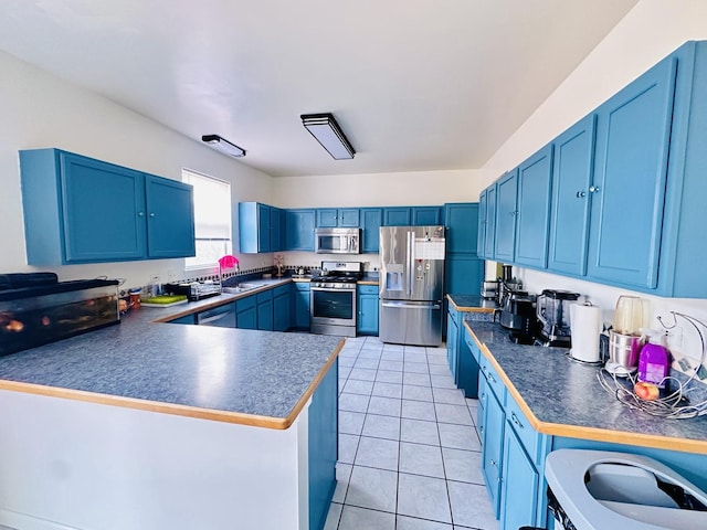 kitchen with light tile patterned floors, appliances with stainless steel finishes, blue cabinets, washer / dryer, and kitchen peninsula