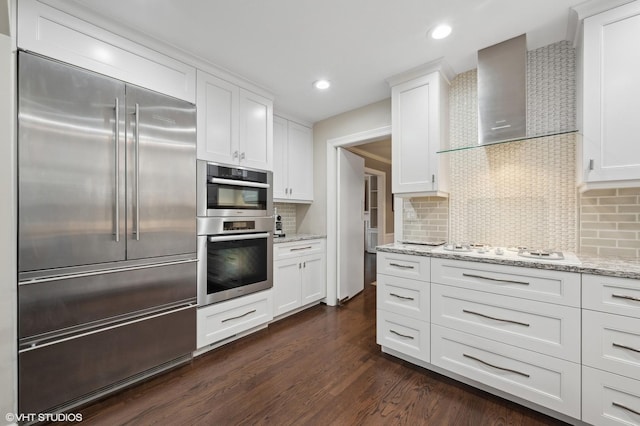 kitchen featuring dark wood-type flooring, wall chimney exhaust hood, white cooktop, white cabinetry, and stainless steel built in fridge