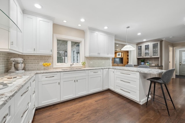 kitchen featuring sink, a breakfast bar area, white cabinetry, decorative light fixtures, and kitchen peninsula