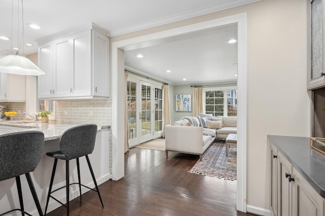 kitchen featuring dark wood-type flooring, hanging light fixtures, light stone countertops, decorative backsplash, and white cabinets