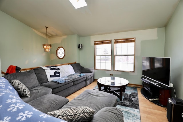 living room featuring an inviting chandelier, lofted ceiling with skylight, and light wood-type flooring