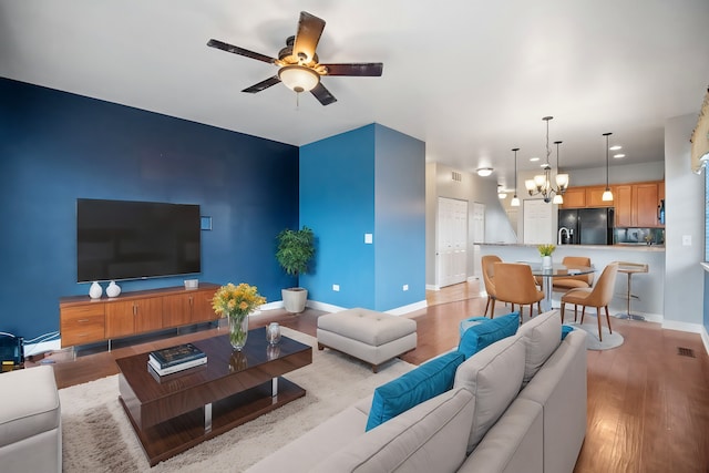 living room featuring ceiling fan with notable chandelier and light hardwood / wood-style flooring