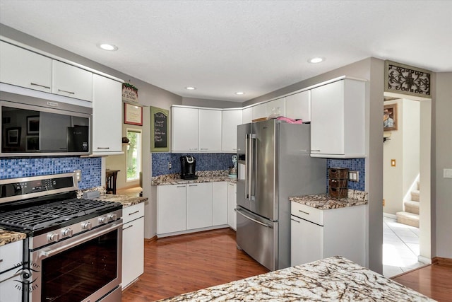 kitchen featuring recessed lighting, stainless steel appliances, wood finished floors, white cabinets, and tasteful backsplash