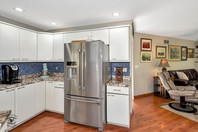 kitchen with open floor plan, high quality fridge, wood finished floors, and white cabinets