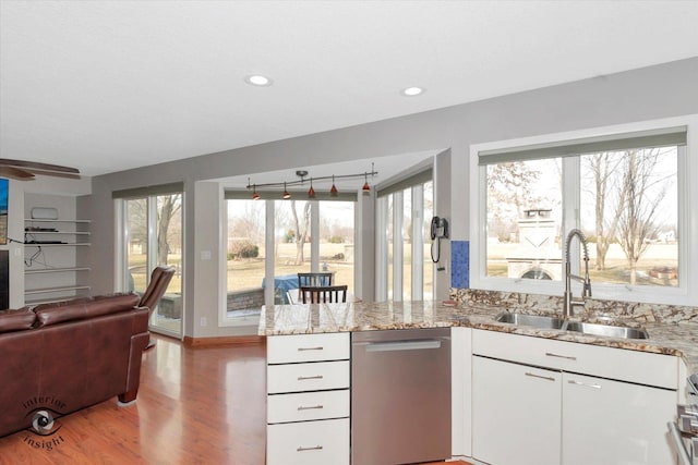 kitchen with a peninsula, stainless steel dishwasher, a sink, and light stone counters