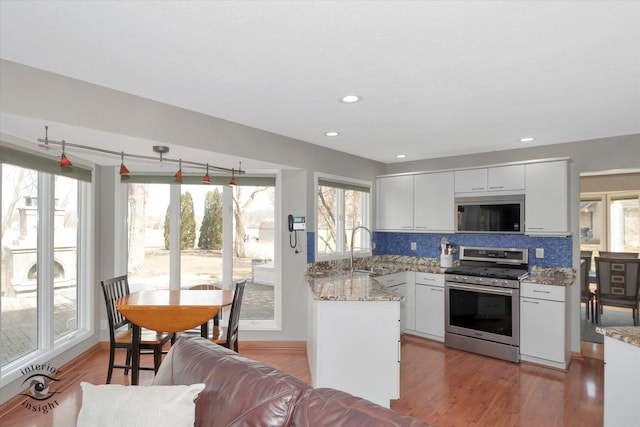 kitchen featuring stainless steel appliances, wood finished floors, a sink, white cabinets, and backsplash