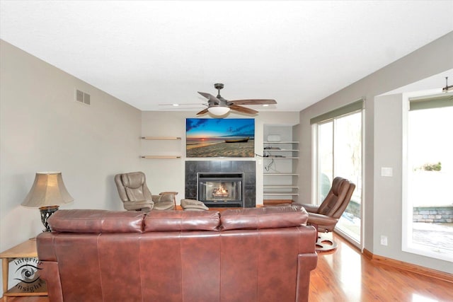 living area featuring visible vents, ceiling fan, wood finished floors, a tile fireplace, and baseboards