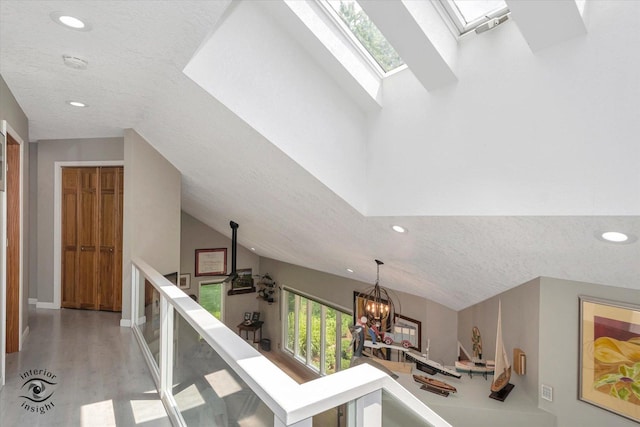 hall with a textured ceiling, recessed lighting, a notable chandelier, a skylight, and an upstairs landing