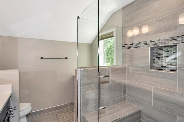 bathroom with baseboards, toilet, lofted ceiling, a tile shower, and vanity