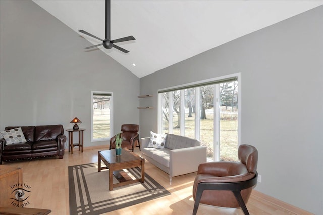 living area featuring light wood finished floors, baseboards, high vaulted ceiling, and a ceiling fan