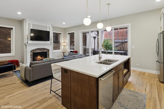 kitchen featuring stainless steel appliances, an island with sink, sink, and light hardwood / wood-style floors